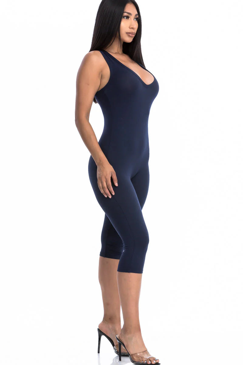 Woman wearing navy sleeveless racer back capri jumpsuit, highlighting high-stretch fabric and slenderizing silhouette.