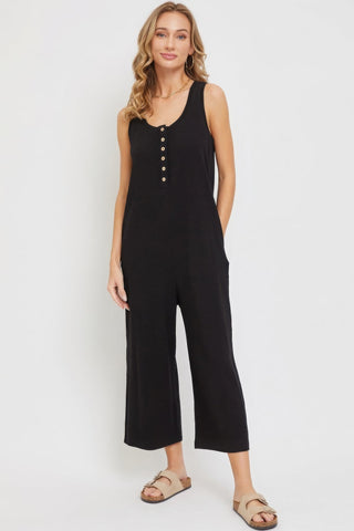 Woman wearing black sleeveless buttondown jumpsuit with side pockets, showcasing relaxed fit and trendy casual style.