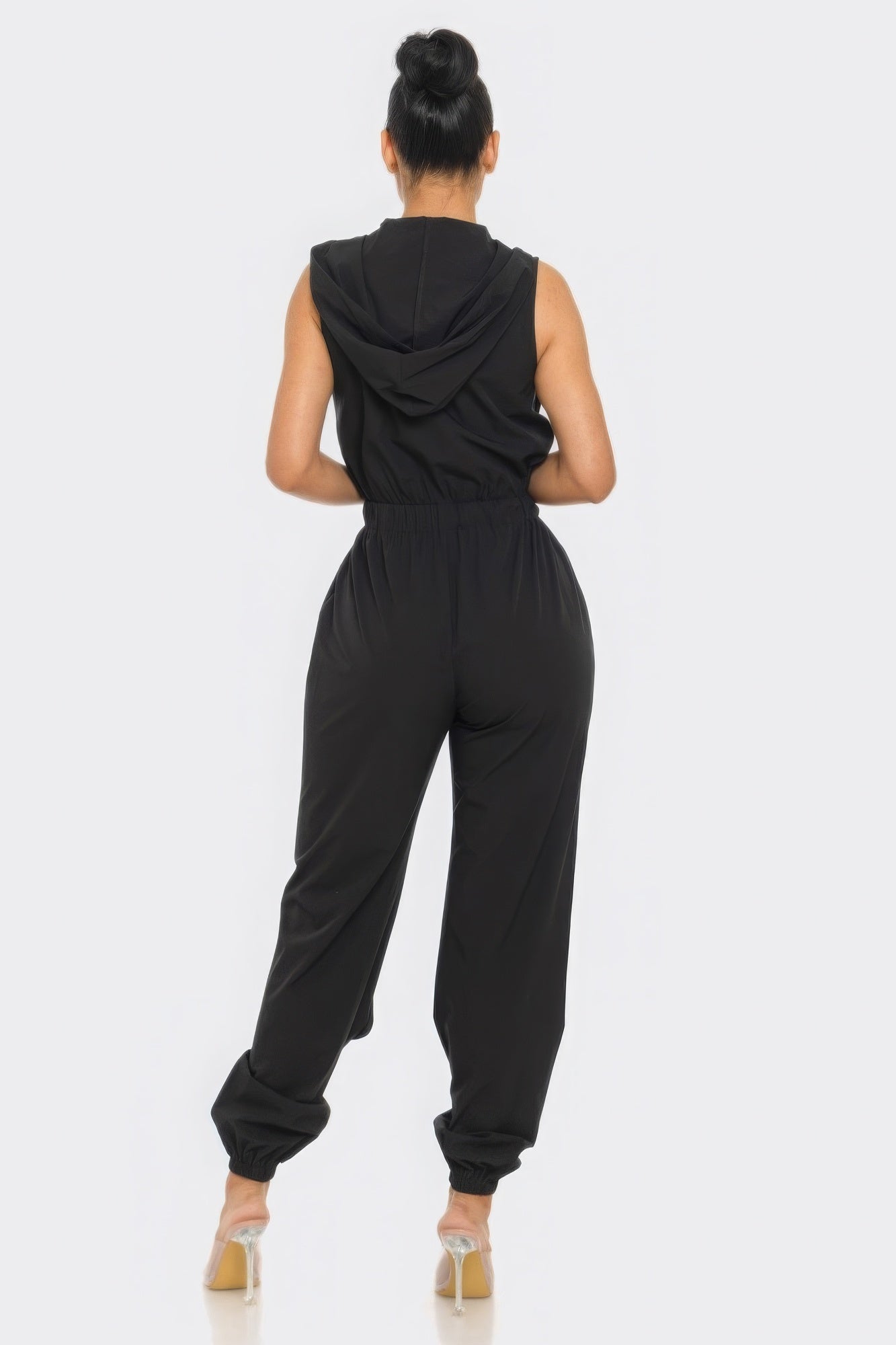 Woman wearing chic black cargo jumpsuit with hoodie, back view, showcasing relaxed fit and zip closure. Perfect for versatile all-day wear.