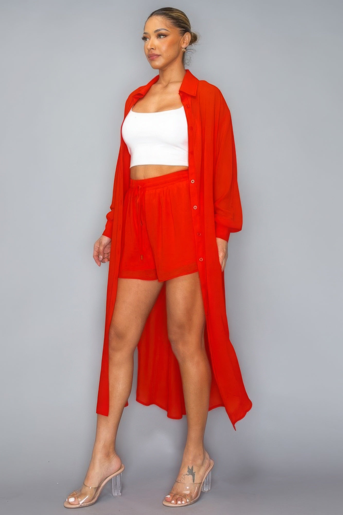 Woman wearing red button down long sleeve side slit two-piece set with shorts and clear heels.