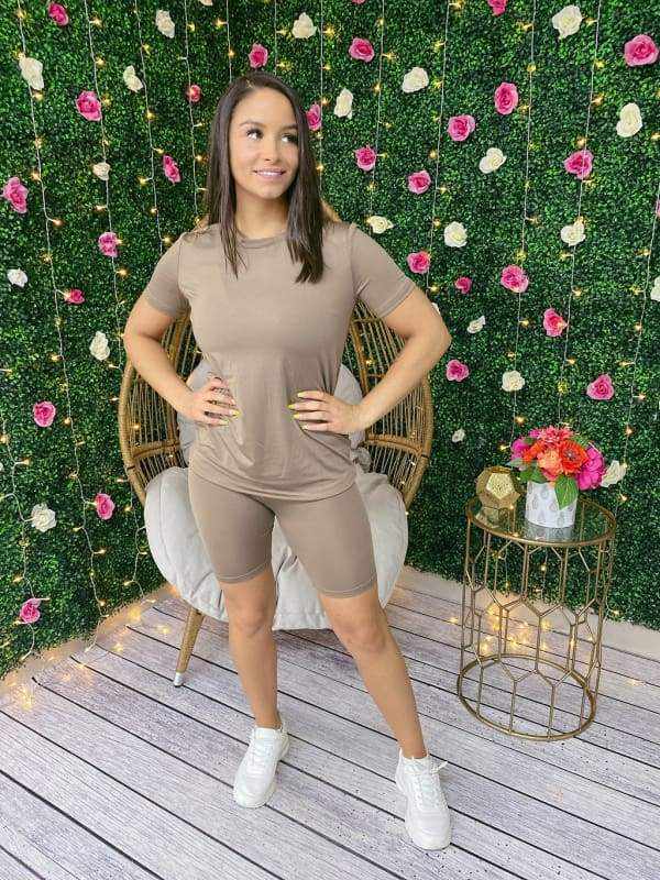 Woman in a Chill Day Biker Short Set stands against floral backdrop, wearing a solid top and shorts made of 96% polyester, 4% spandex.