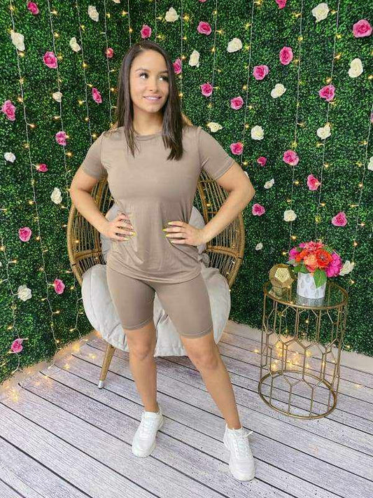 Woman in a Chill Day Biker Short Set stands against floral backdrop, wearing a solid top and shorts made of 96% polyester, 4% spandex.