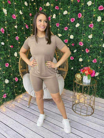 Woman in a Chill Day Biker Short Set stands against floral backdrop, wearing a solid top and shorts made of 96% polyester, 4% spandex.