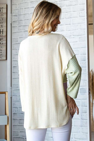 Woman wearing a color block round neck dropped shoulder blouse in a cozy room setting, showcasing back design.