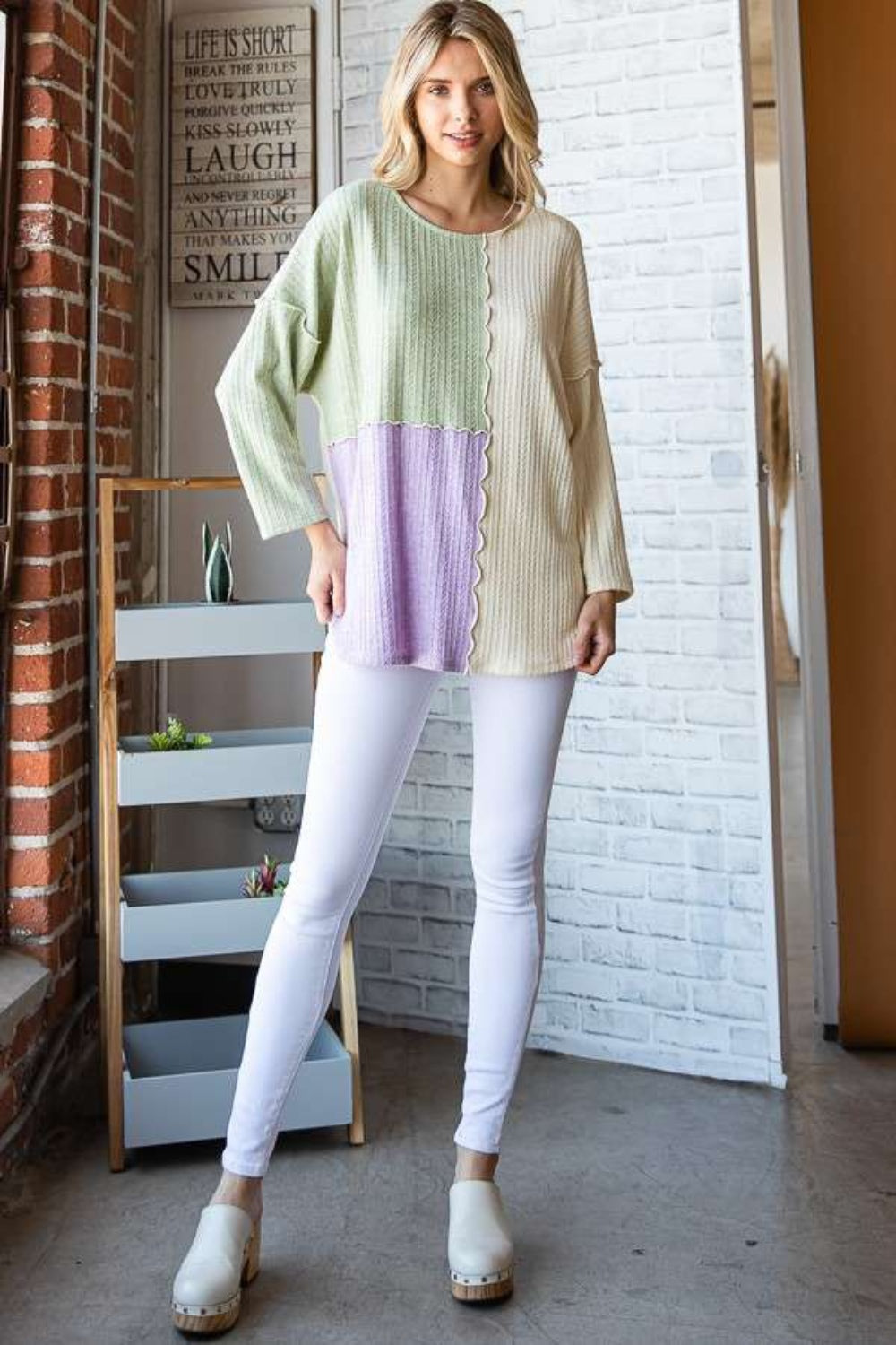 Woman wearing a color block round neck dropped shoulder blouse with white leggings, showcasing a casual and chic look.