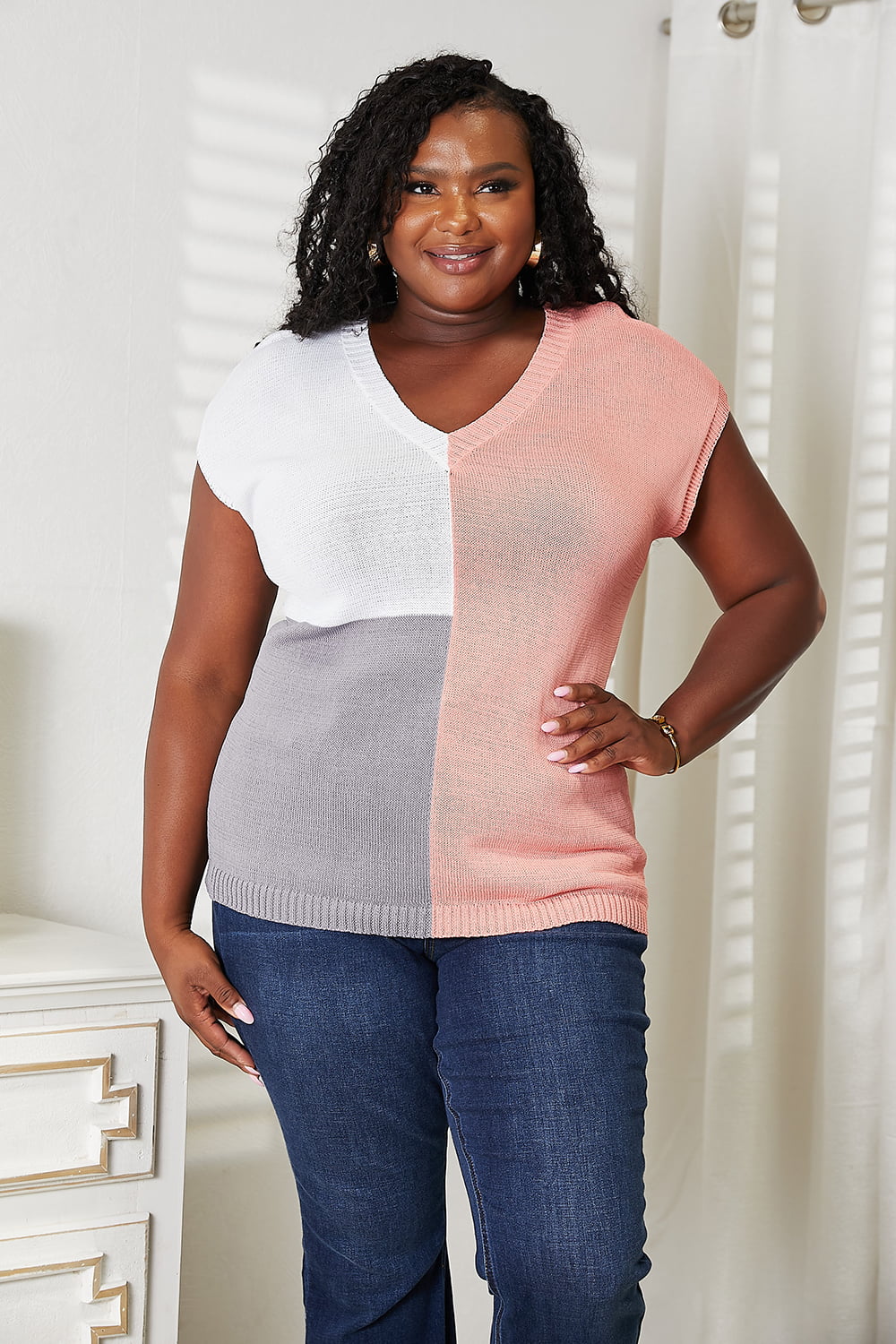 Woman wearing a color block V-neck knit top with short sleeves, featuring a chic and modern design in soft cotton-polyester blend.