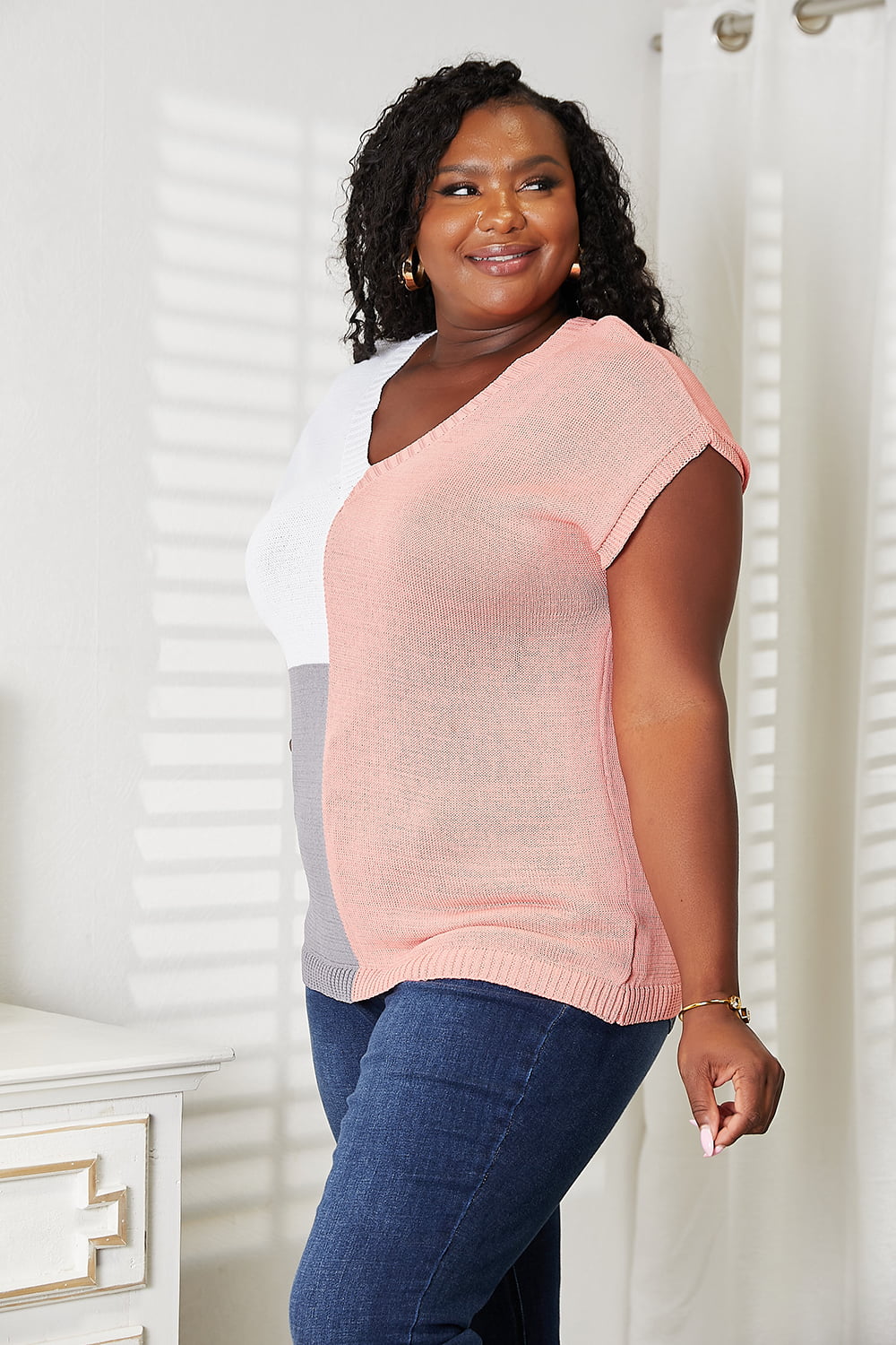 Woman wearing a chic color block V-neck knit top with short sleeves, styled with jeans, standing indoors.