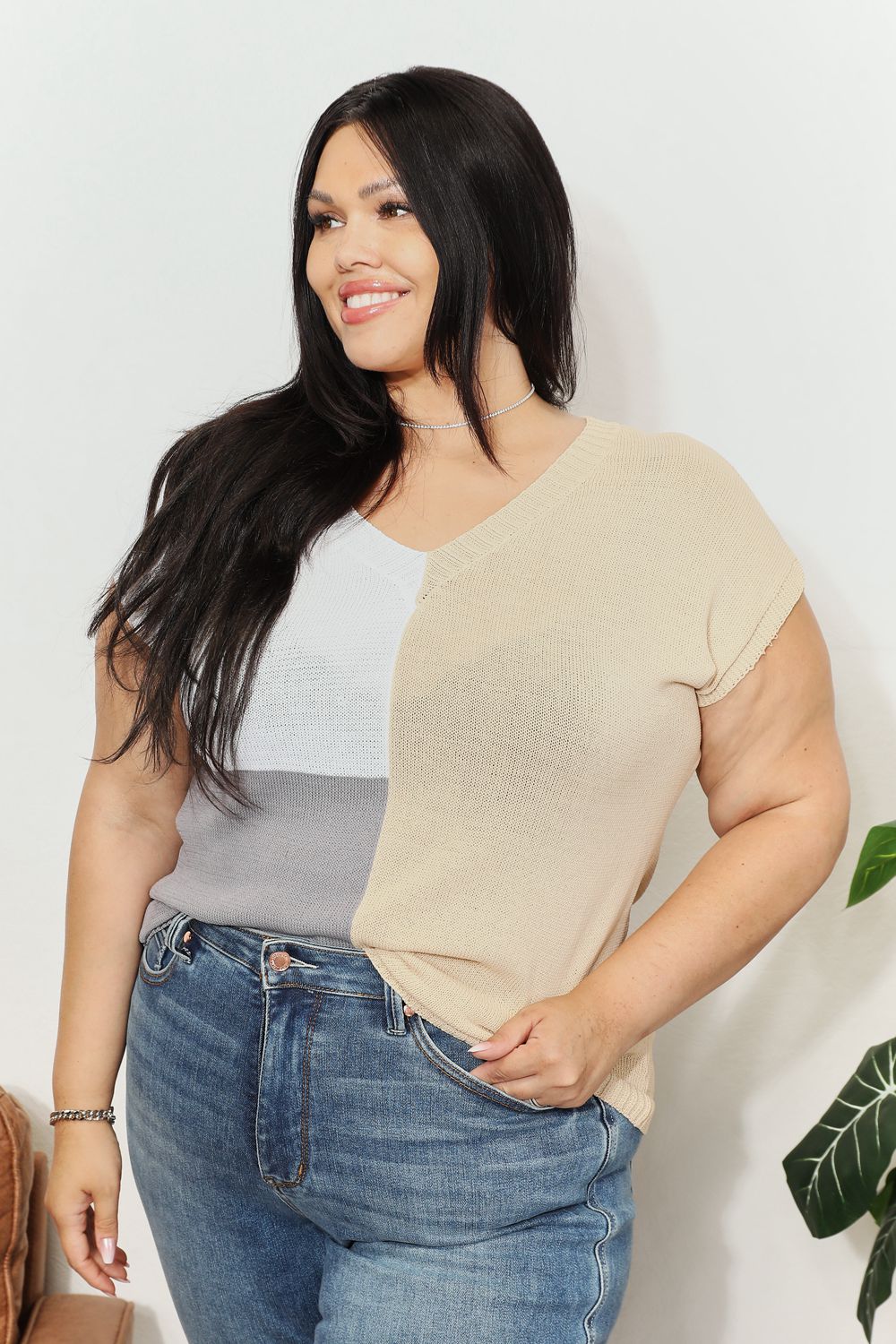 Woman wearing a chic color block V-neck knit top with short sleeves, styled with jeans, showcasing a casual yet sophisticated look.