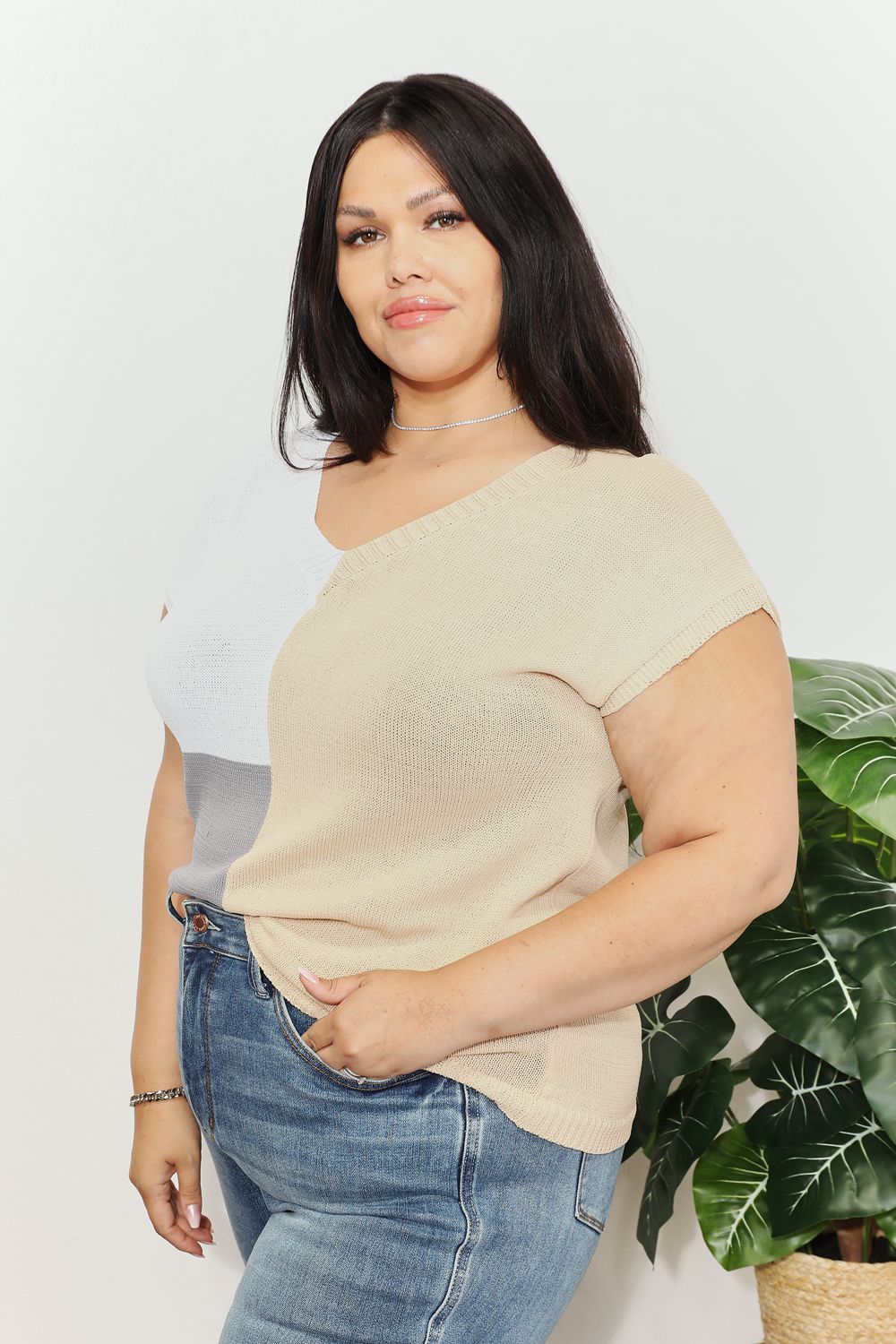 Woman wearing color block V-neck knit top with short sleeves and jeans, styled with chic, modern flair.