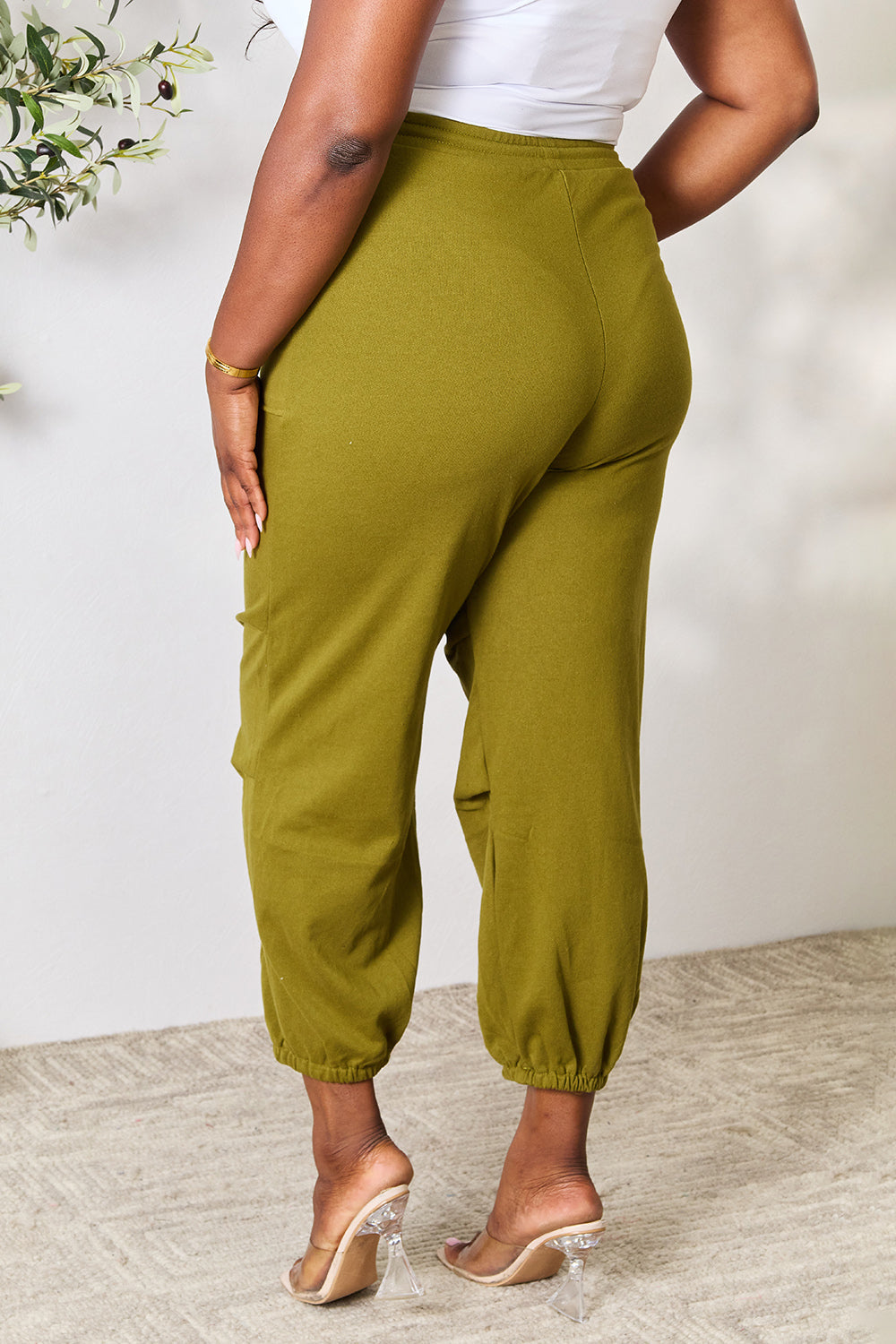 Woman wearing olive green drawstring sweatpants with pockets, basic style in cotton-polyester blend, paired with clear heels.