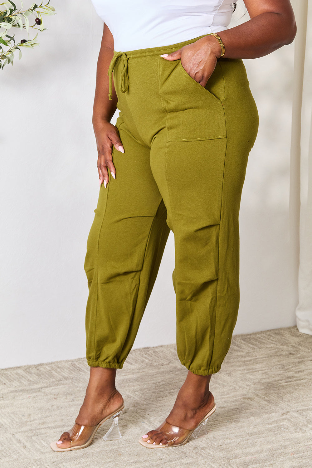 Woman wearing olive green drawstring sweatpants with pockets, basic style, made of 60% cotton and 40% polyester, showcasing comfort.