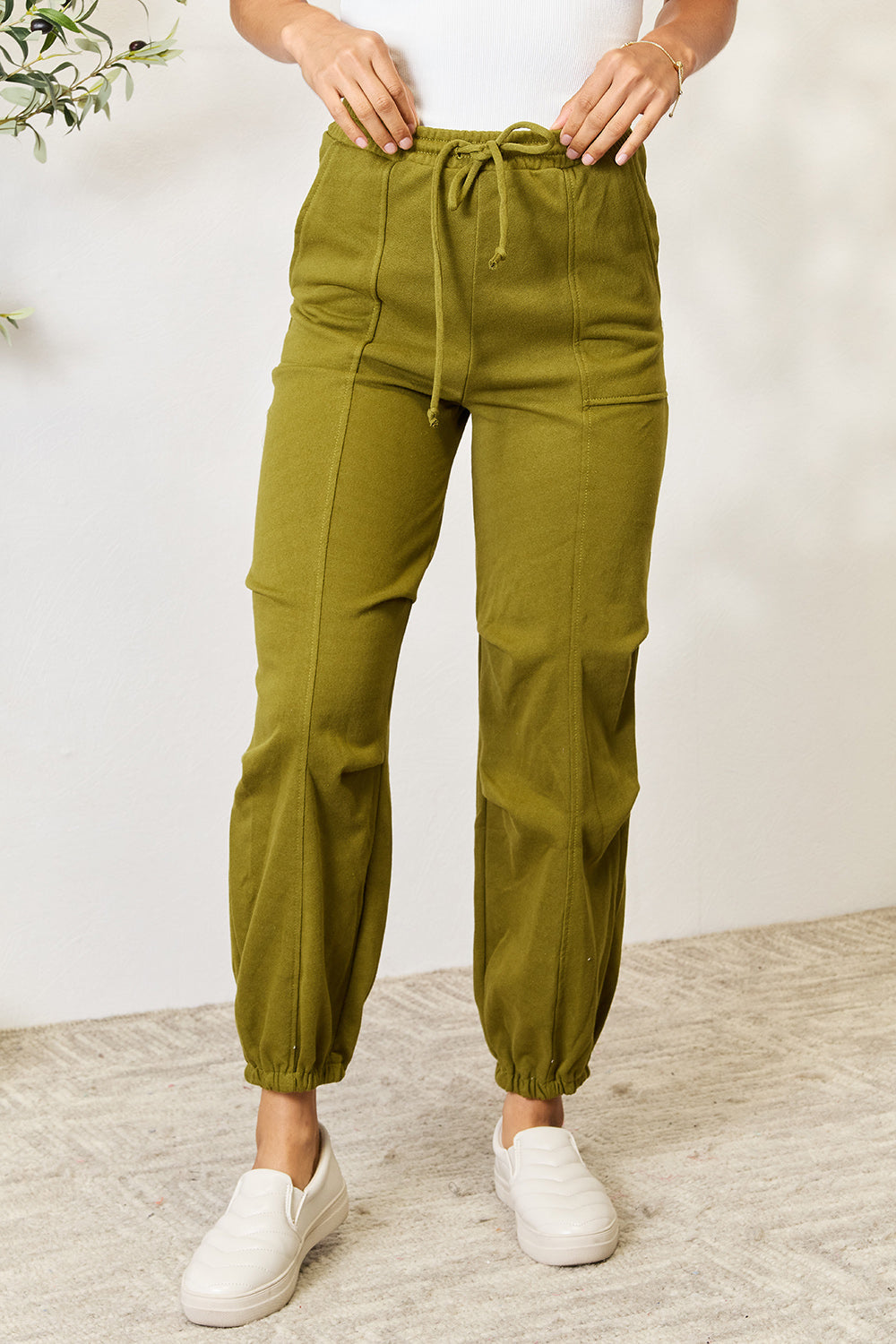 Olive green drawstring sweatpants with pockets, featuring a comfortable fit, made of 60% cotton and 40% polyester.