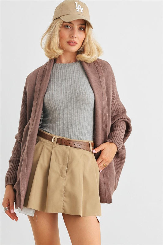 Woman wearing a cocoa batwing sleeve open front cardigan over a gray top and beige skirt, styled casually with a baseball cap.