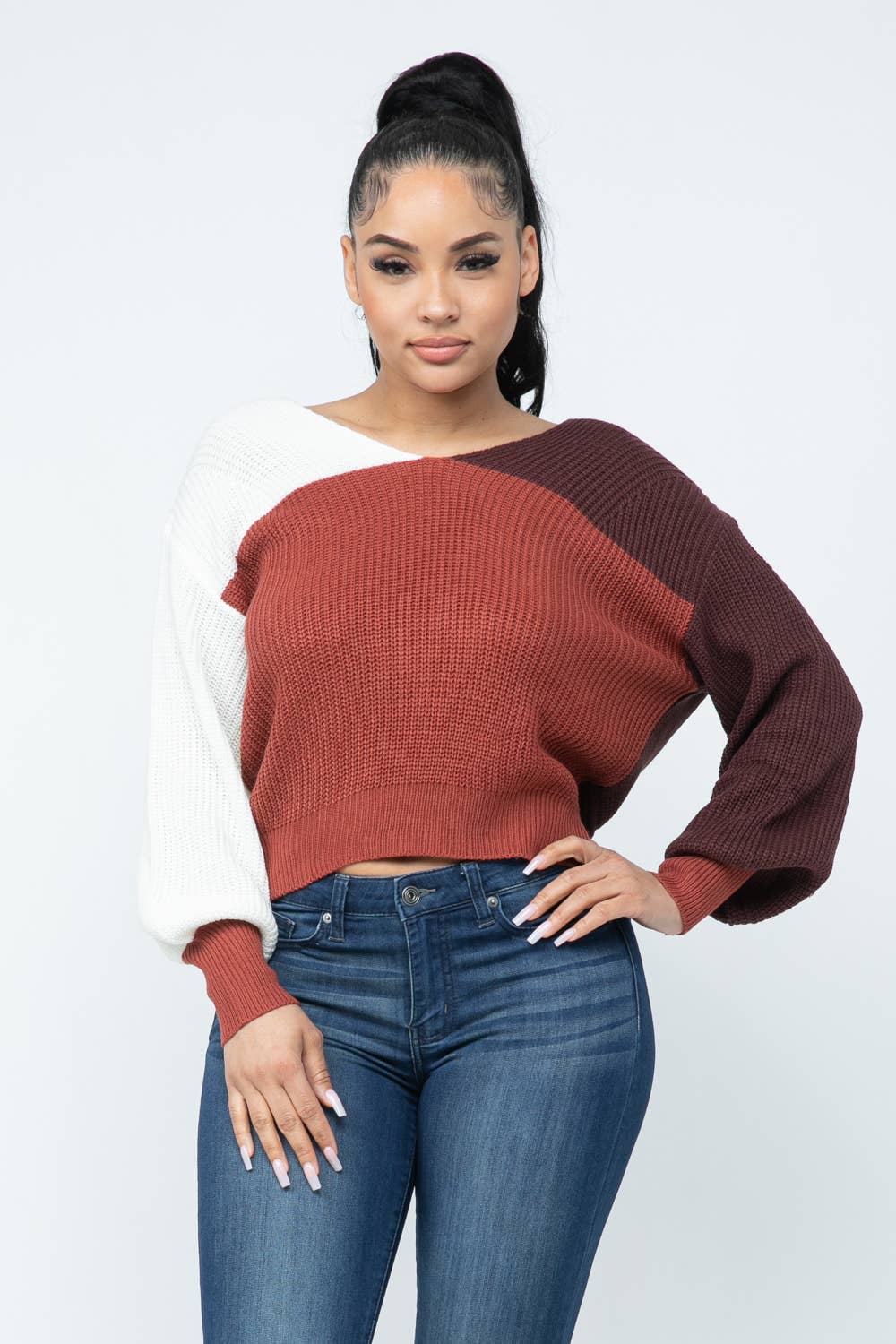 Woman wearing a color block twisted open back loose fit cozy sweater in red, white, and brown with jeans, showcasing casual fashion.