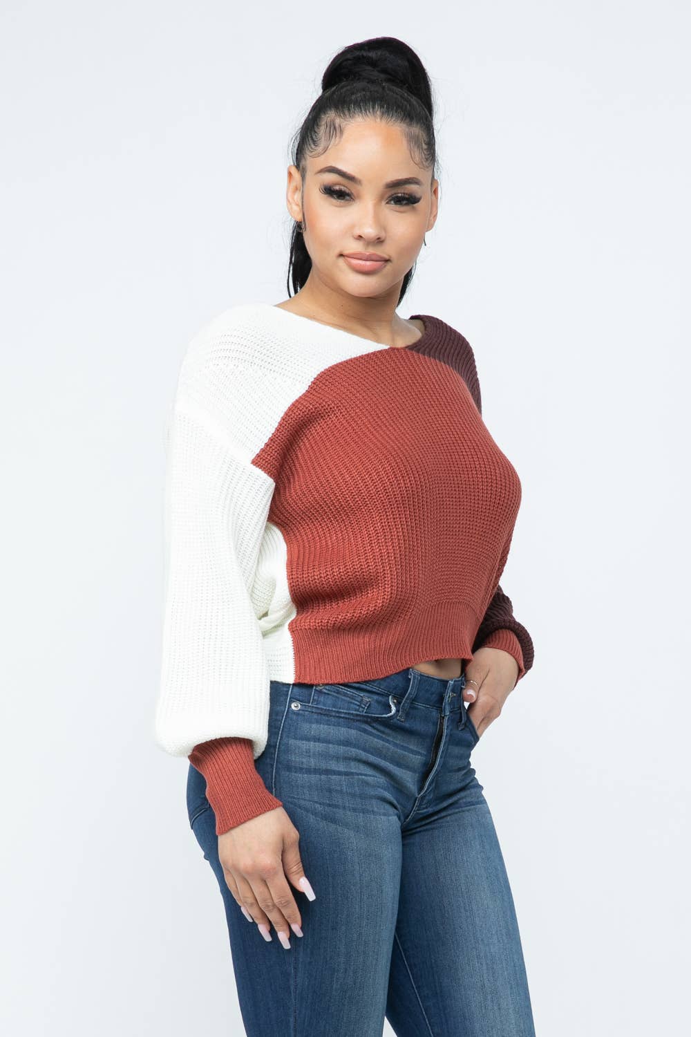 Woman wearing color block twisted open back loose fit cozy sweater in red and white, paired with jeans.