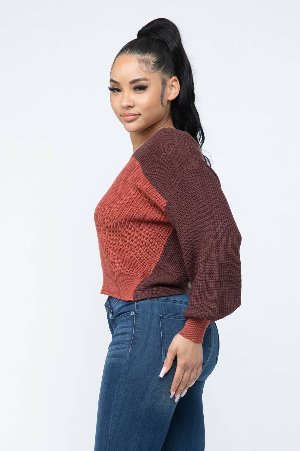 Woman wearing a color block twisted open back cozy sweater in side view.