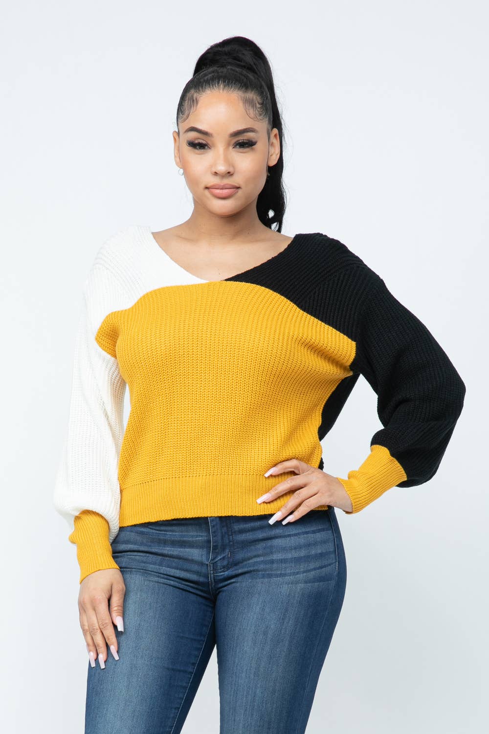 Woman wearing color block twisted open back cozy sweater with yellow, black, and white sections, paired with jeans, showcasing loose fit.