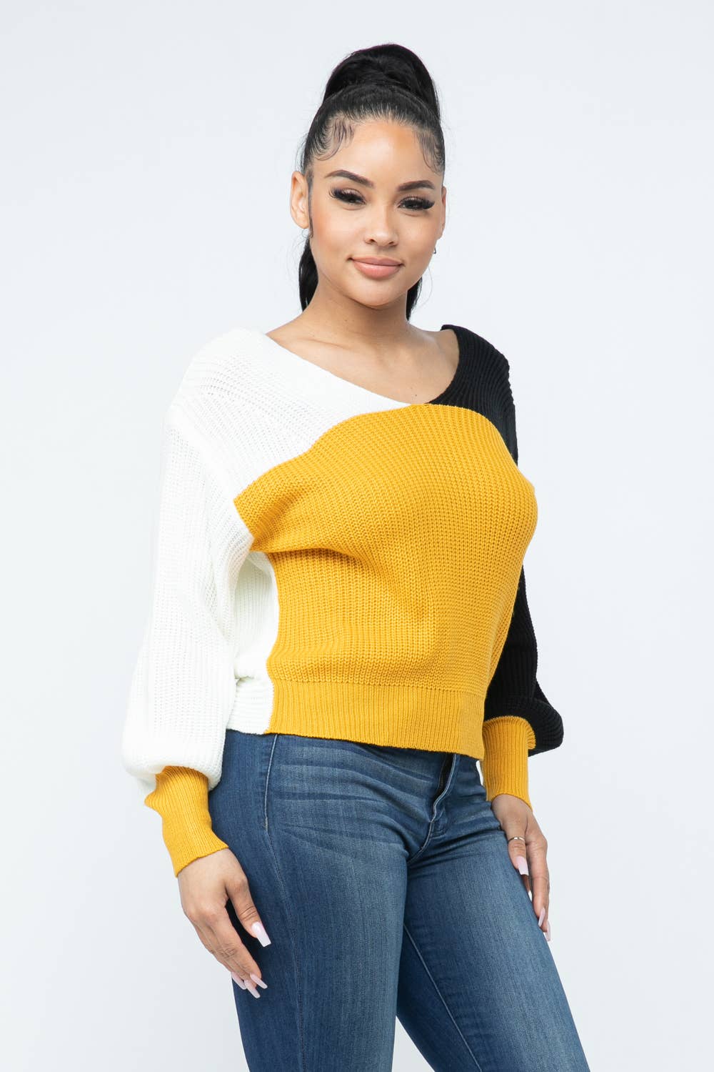 Woman wearing color block twisted open back cozy sweater in mustard, black, and white, perfect for a stylish and comfortable look.