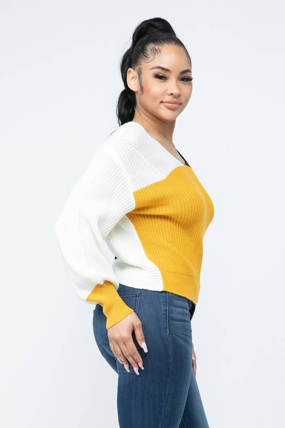 Woman wearing color block twisted open back loose fit cozy sweater in yellow and white.