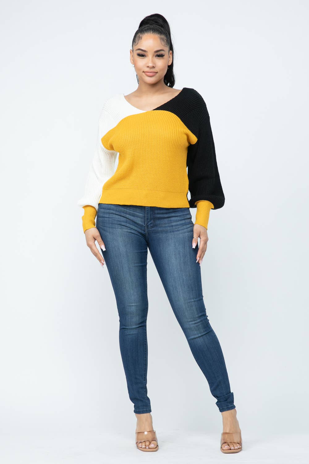 Woman wearing color block twisted open back loose fit cozy sweater in yellow, black, and white with jeans.