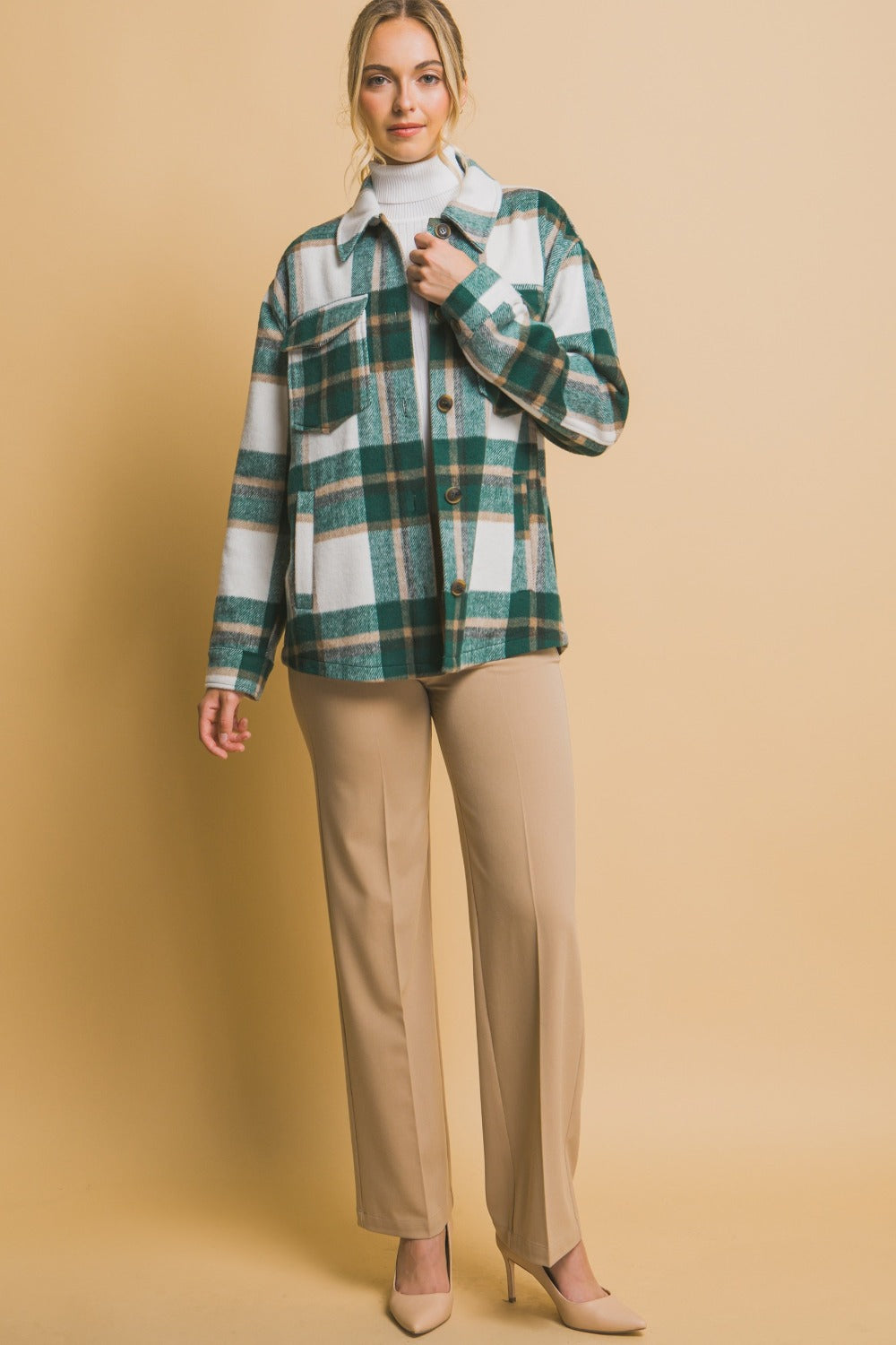 Woman wearing green plaid button-up shacket with pockets, made from 100% polyester, paired with beige pants and heels.