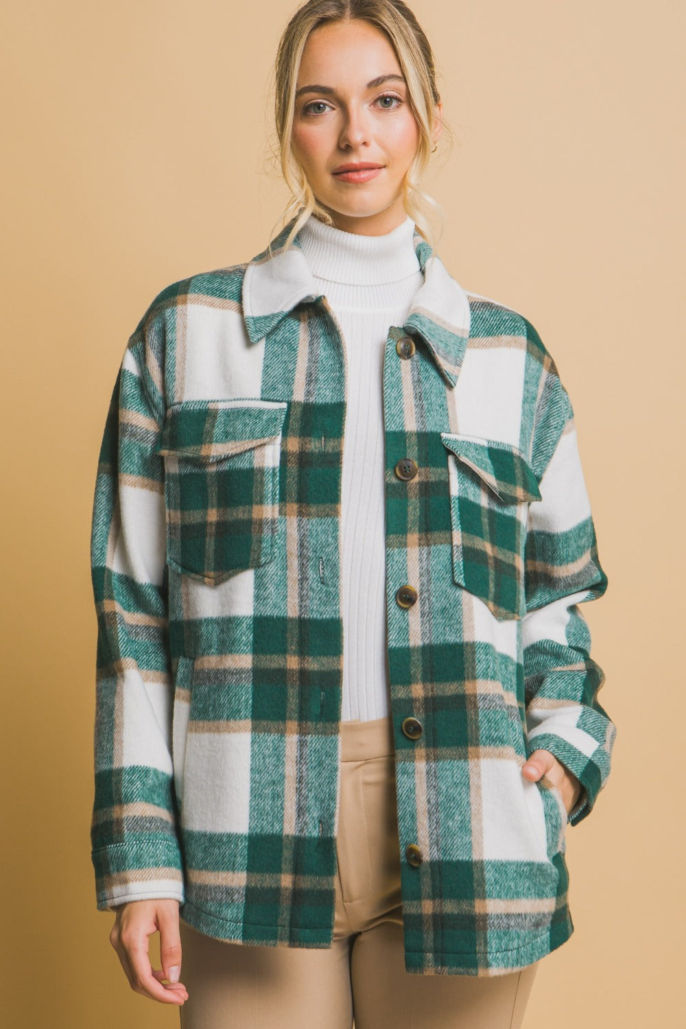 Woman wearing green plaid button-up shacket with pockets, 100% polyester, not lined, over white turtleneck and beige pants.