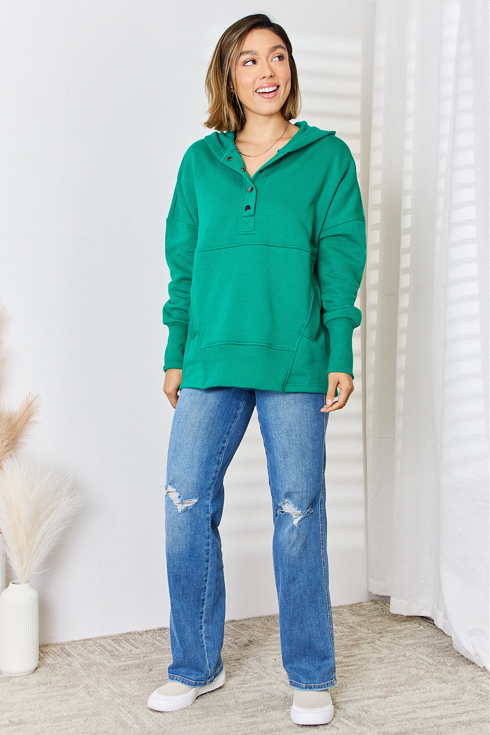 Woman wearing green half snap long sleeve hoodie paired with blue jeans, showcasing casual fashion style.