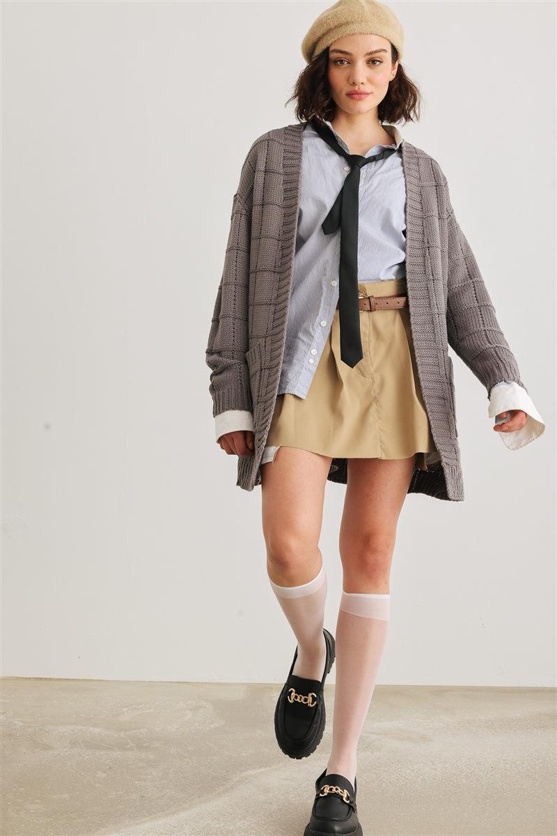 Woman wearing a heather charcoal knit two pocket long sleeve cardigan over a shirt and skirt outfit with a beret and loafers.