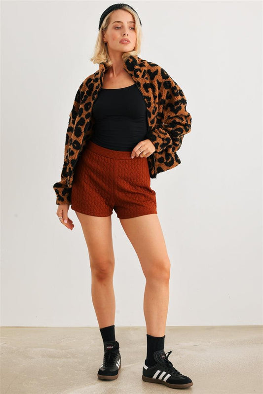 Woman wearing a leopard print teddy jacket with two pockets and a zipper, styled with shorts and sneakers, standing indoors.