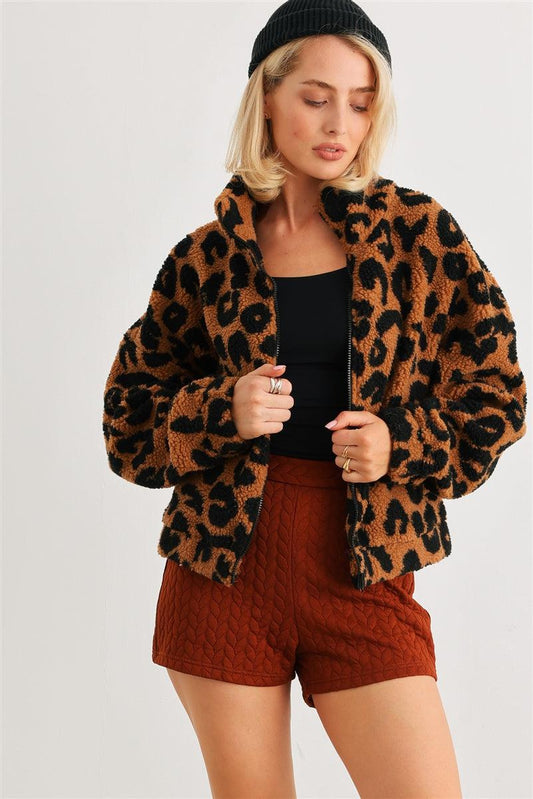 Woman wearing a cozy leopard print teddy jacket with front zip and two pockets, styled with a black top and rust shorts, casual look.