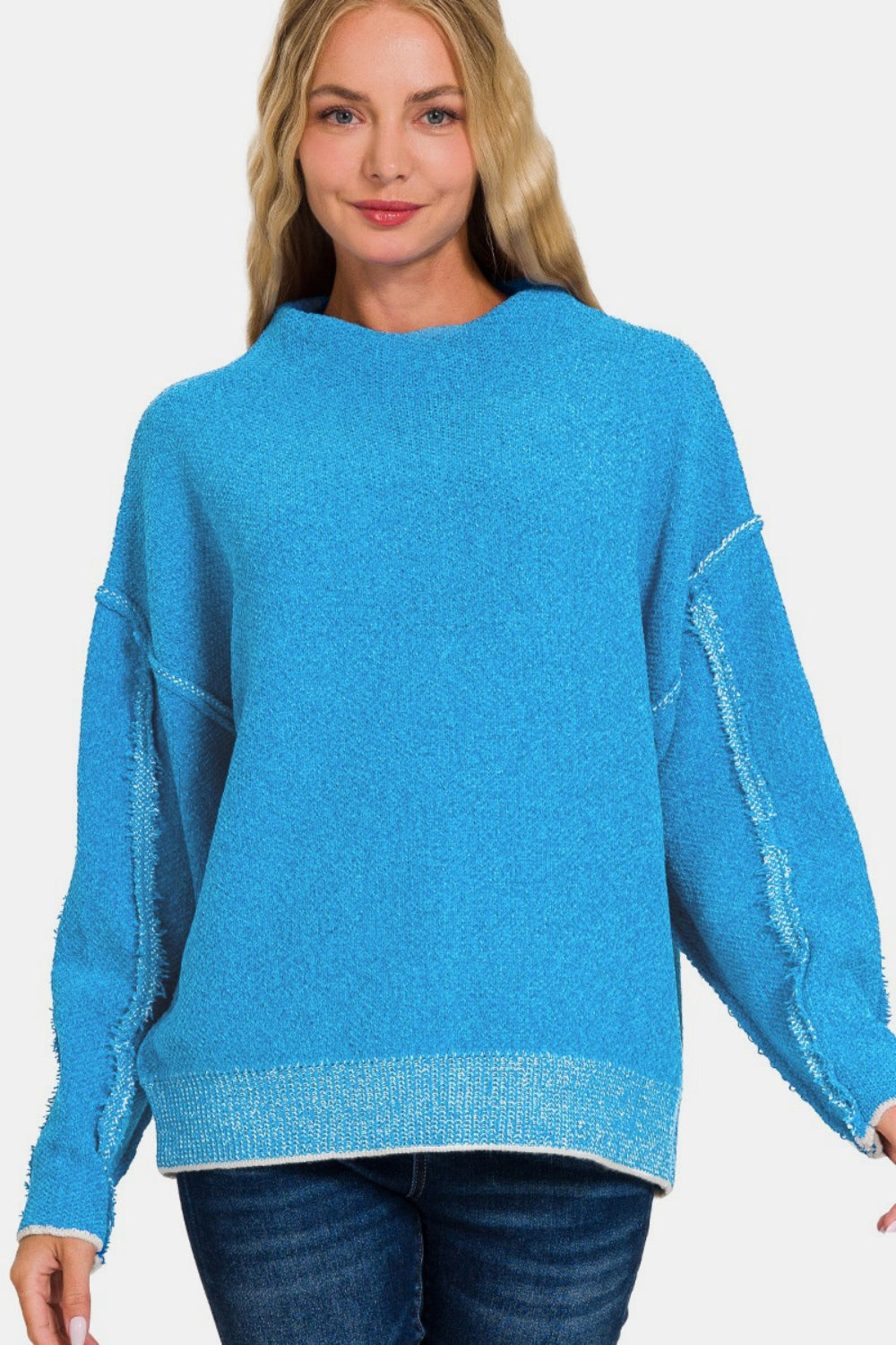 Woman wearing a cozy blue exposed seam mock neck long sleeve sweater with slightly stretchy fabric, made of 79% polyester and 21% acrylic.