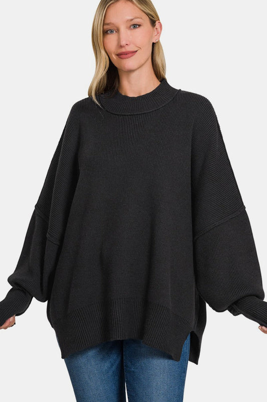 Oversized black sweater with exposed seams and side slits, modeled with jeans for a cozy, casual look.