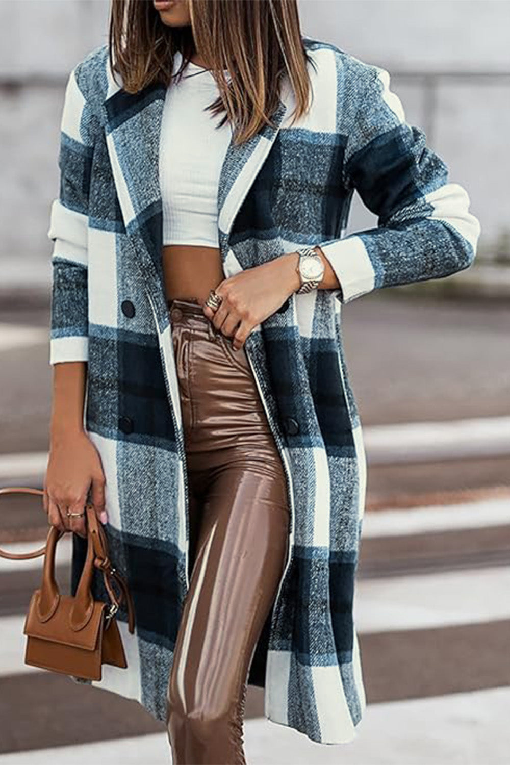 Woman wearing full size plaid button up lapel collar coat with brown pants and carrying a small handbag outdoors.