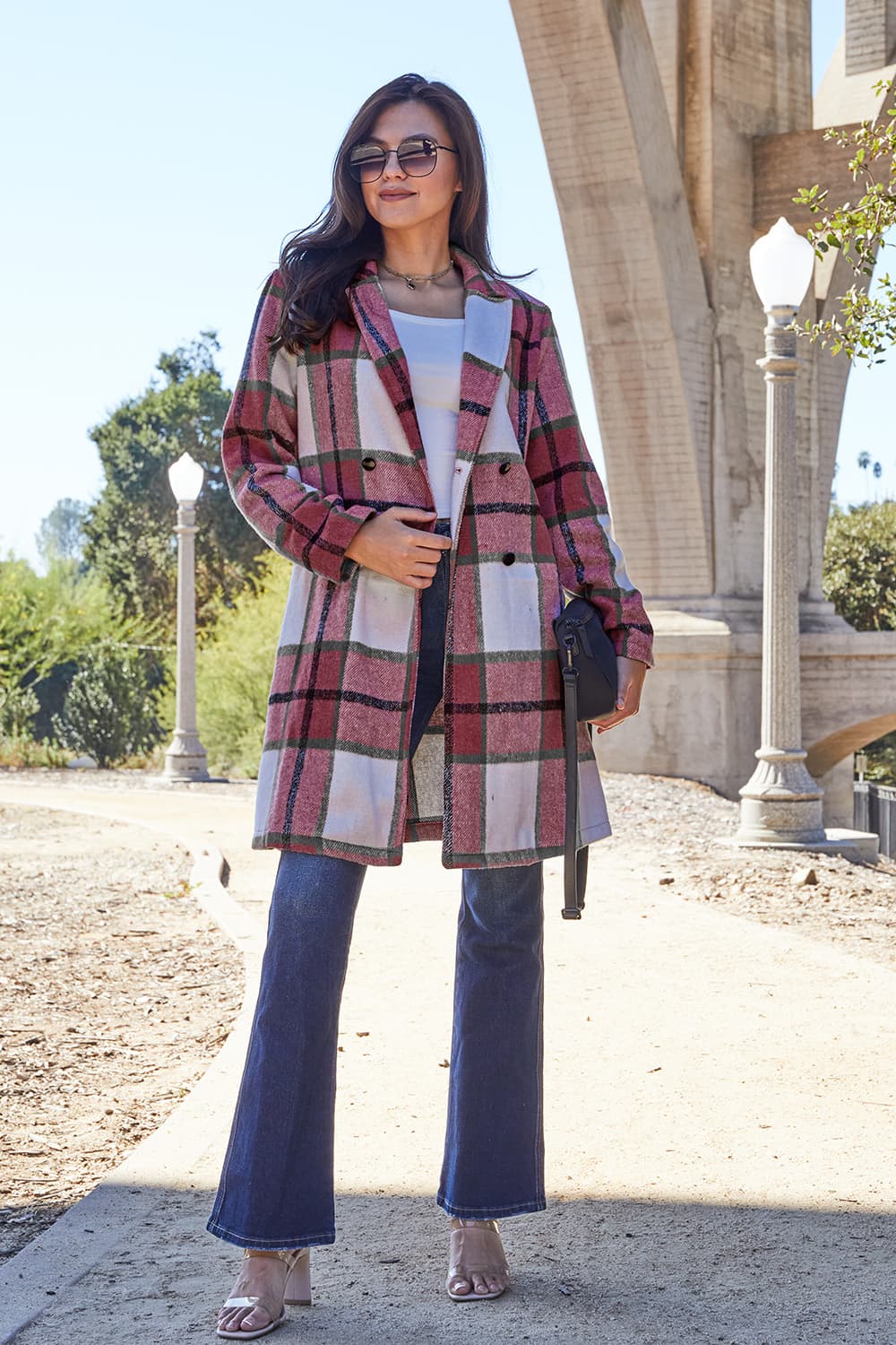 Woman wearing a full size plaid button up lapel collar coat with pockets, standing outdoors on a sunny day.