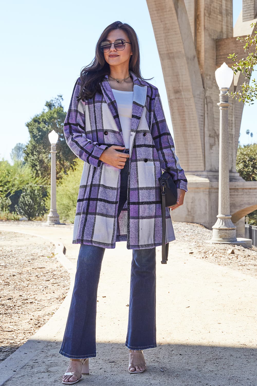 Woman wearing full size plaid button-up lapel collar coat with pockets, outdoors under a bridge.