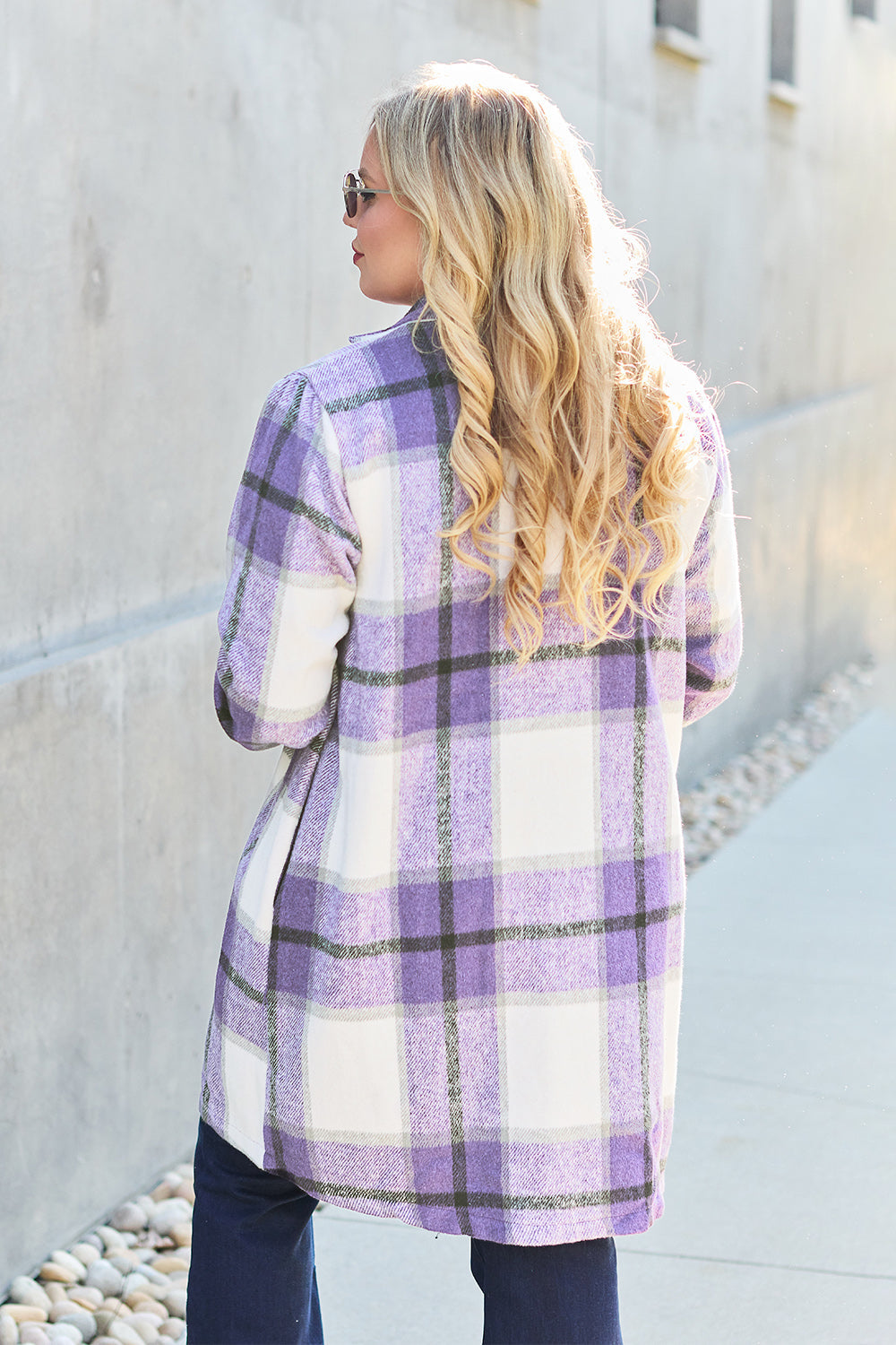 Woman wearing purple plaid button-up lapel collar coat made of 100% polyester with pockets, sidewalk background.