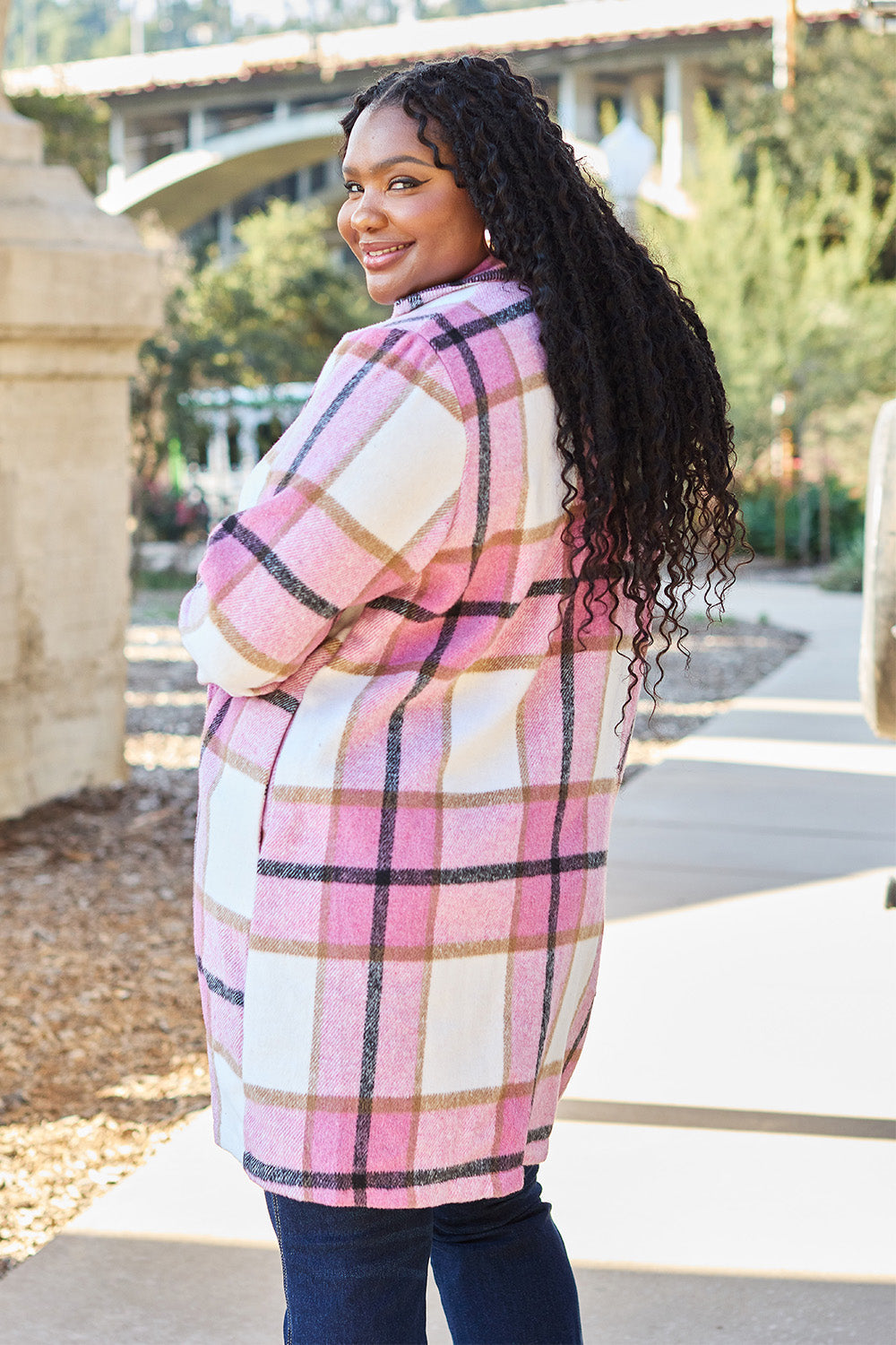 Woman wearing a full size plaid button-up coat with lapel collar, featuring pink and white checks, and smiling outdoors.