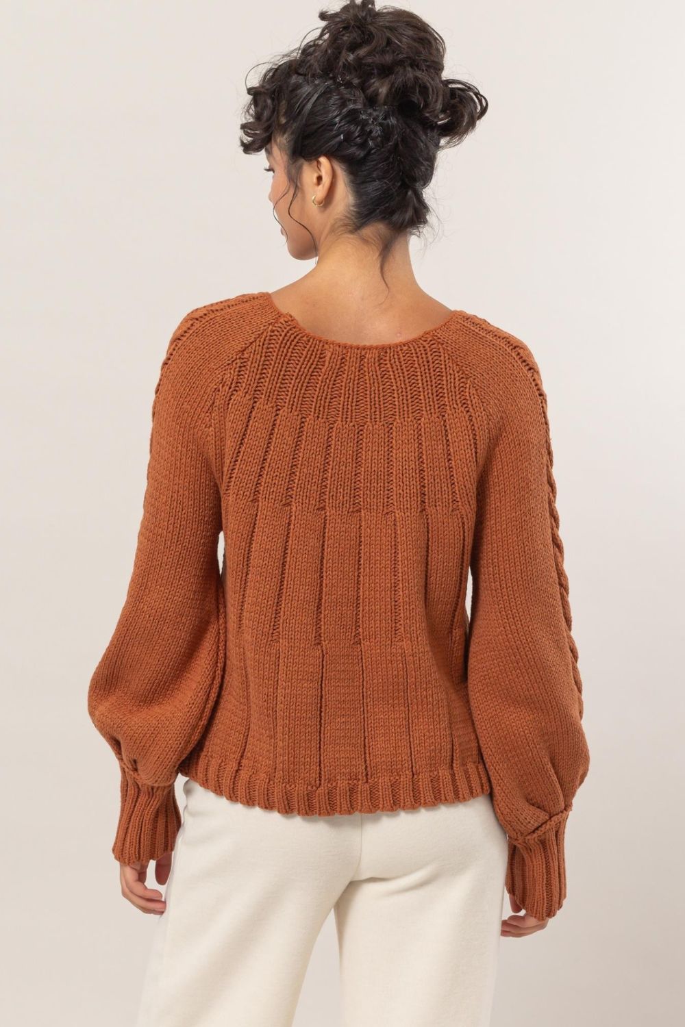 Woman wearing a HYFVE cable-knit round neck raglan sleeve sweater in rust color, showcasing the back design.