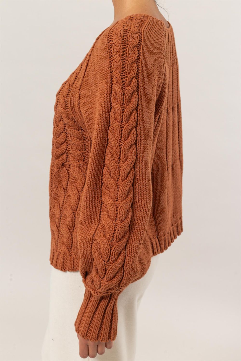 Side view of HYFVE cable-knit round neck raglan sleeve sweater in rust color, showcasing detailed knit texture and design.