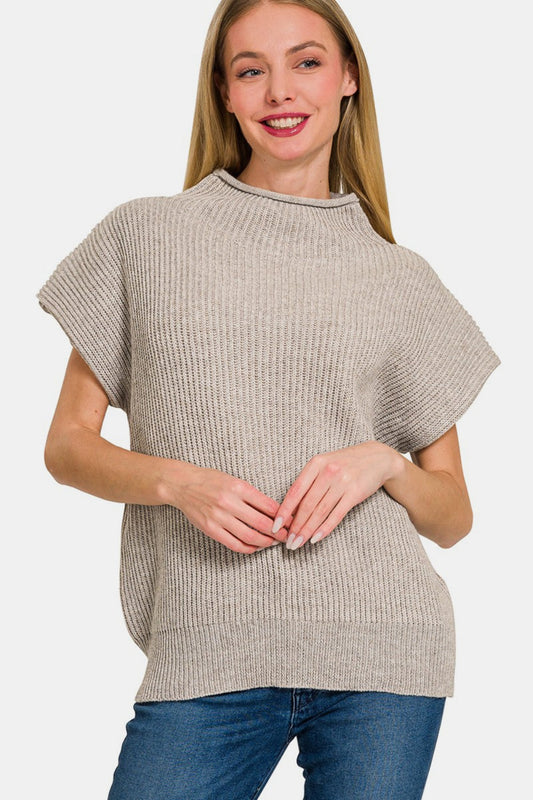 Woman wearing a short sleeve mock neck sweater in a neutral color, made from 50% polyester and 50% acrylic, paired with jeans.