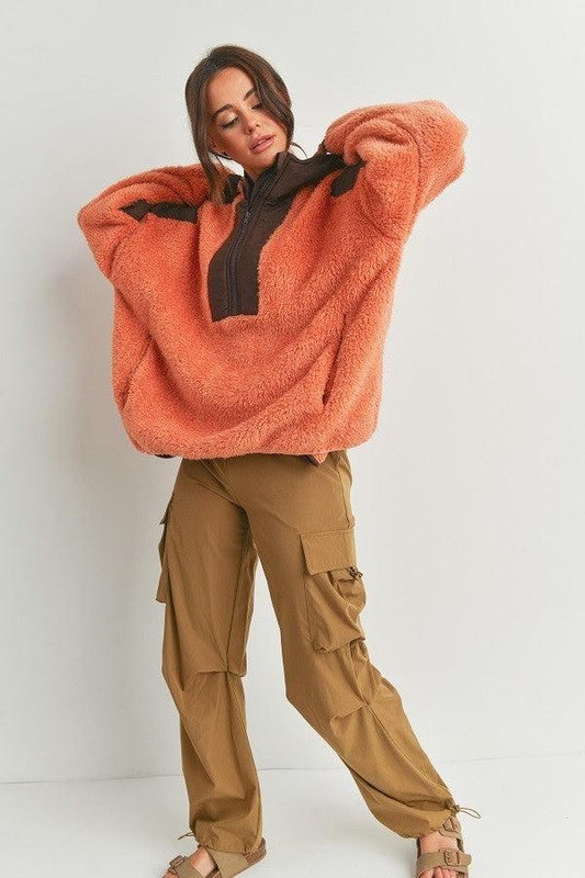 Woman wearing a cozy two-toned hooded sweater in orange and brown with cargo pants, showcasing a comfortable and stylish look.