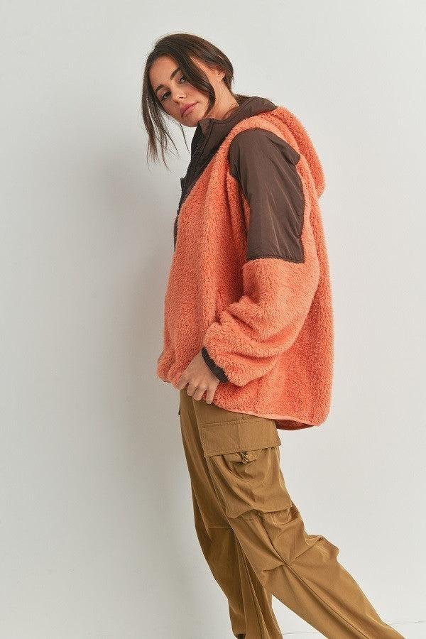 Woman wearing a cozy two-toned hooded sweater in orange and brown, paired with khaki pants.