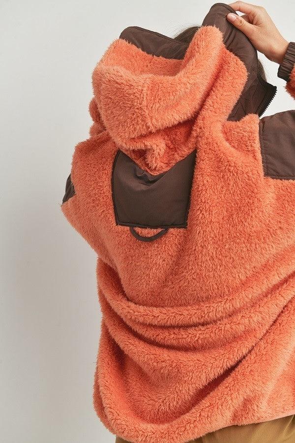 Two-toned cozy hooded sweater in orange and brown, featuring a soft plush texture and stylish design, made of 100% polyester.