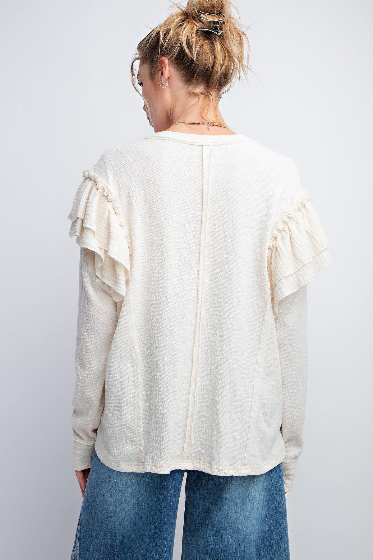 Woman wearing cream double ruffle sleeves top with rounded neckline and relaxed fit, featuring center back seam and dropped shoulders.