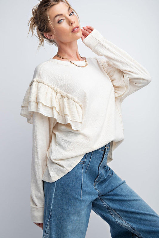 Woman wearing cream double ruffle sleeves top with rounded neckline and relaxed fit, paired with blue jeans.