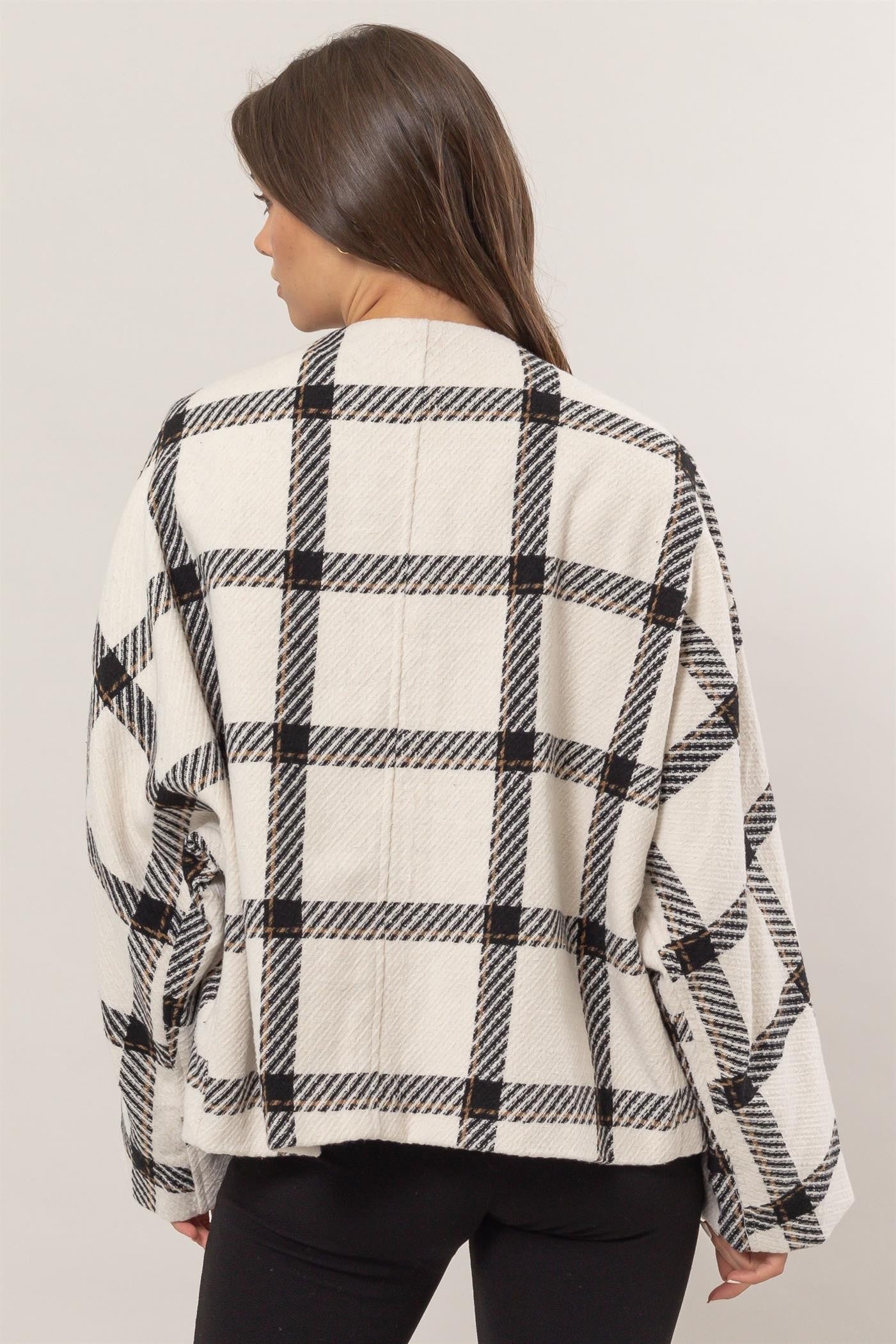 Woman wearing a cream plaid long sleeve jacket with side slit pockets, showcasing its buttoned and lined design made of 100% polyester.