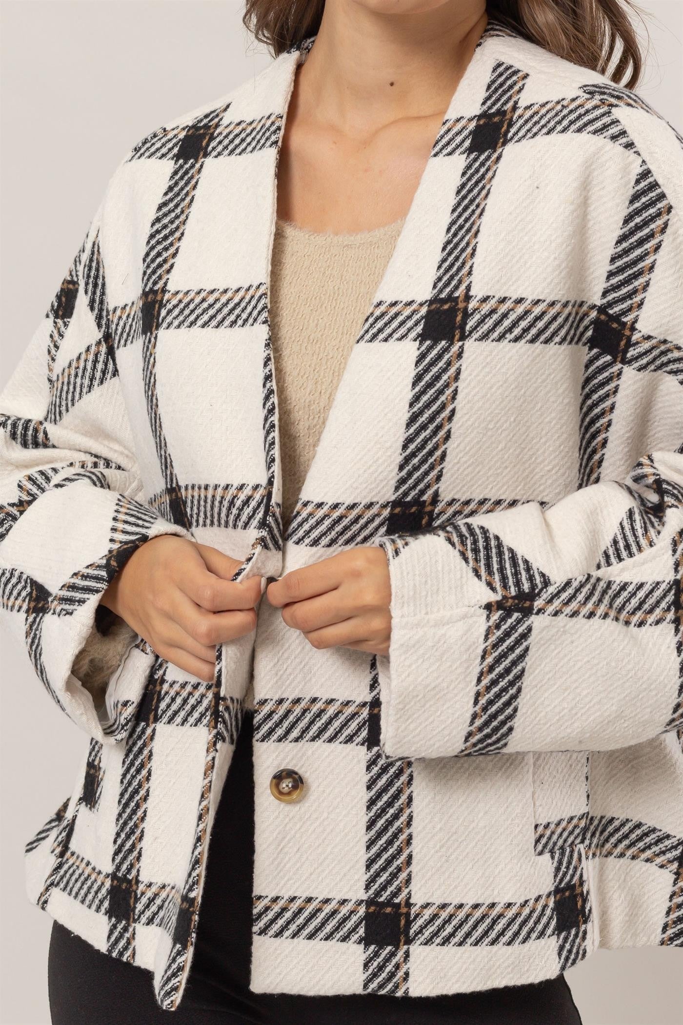 Woman wearing a cream plaid long sleeve jacket with button closure and side slit pockets, made from 100% polyester.