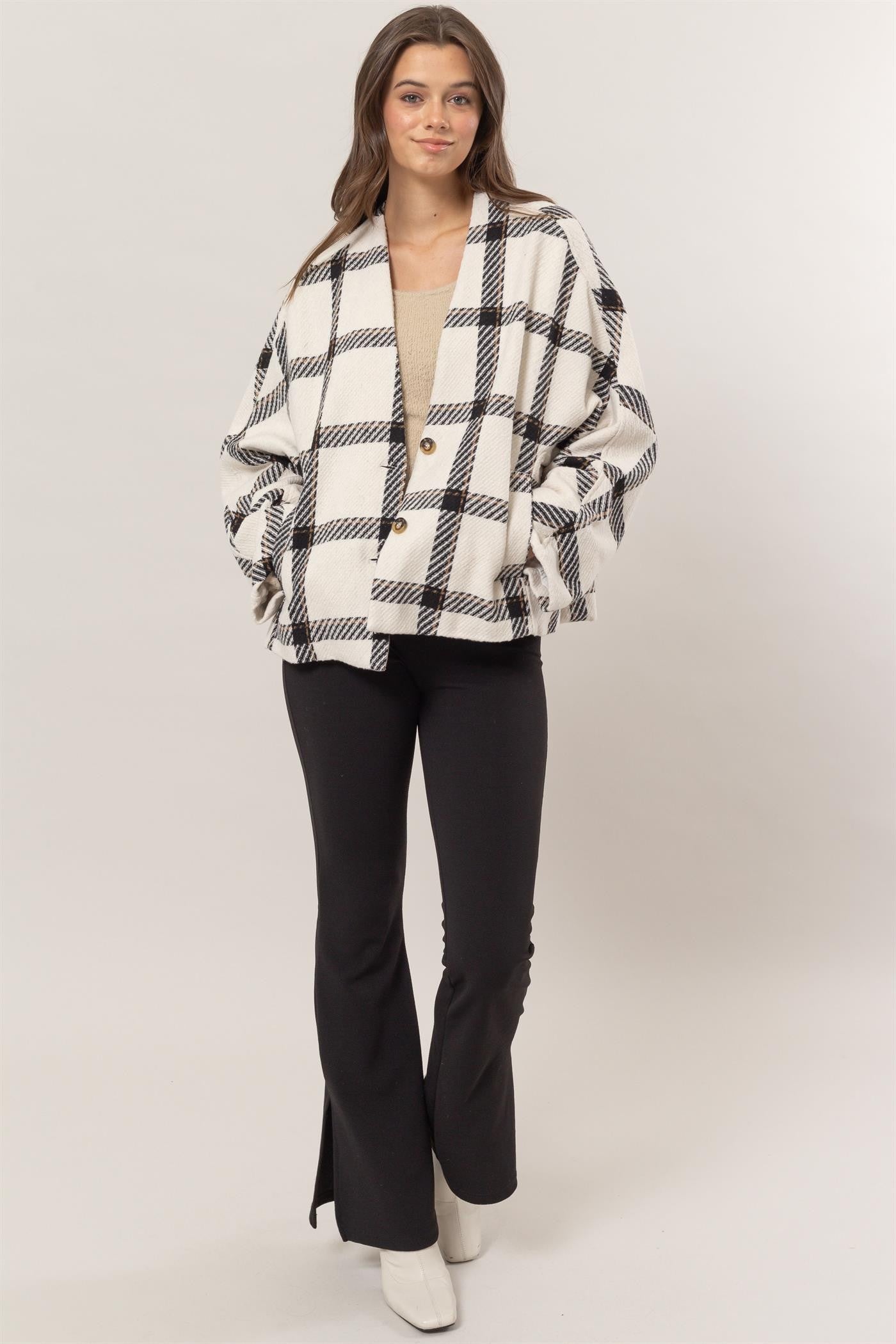 Woman wearing cream plaid long sleeve jacket with side slit pockets, buttoned front, lined with polyester, paired with black pants.