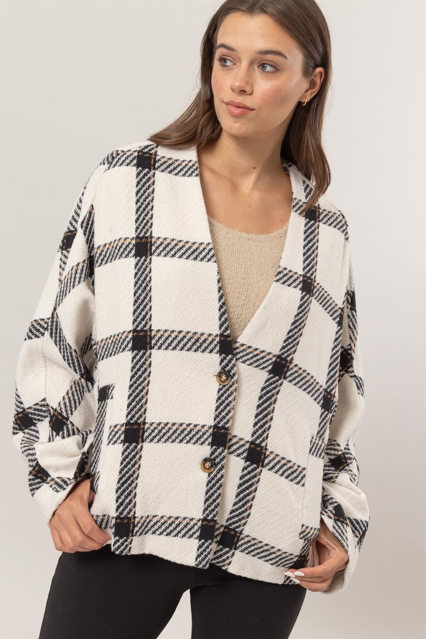 Woman wearing cream plaid long sleeve jacket with buttoned design and side slit pockets.