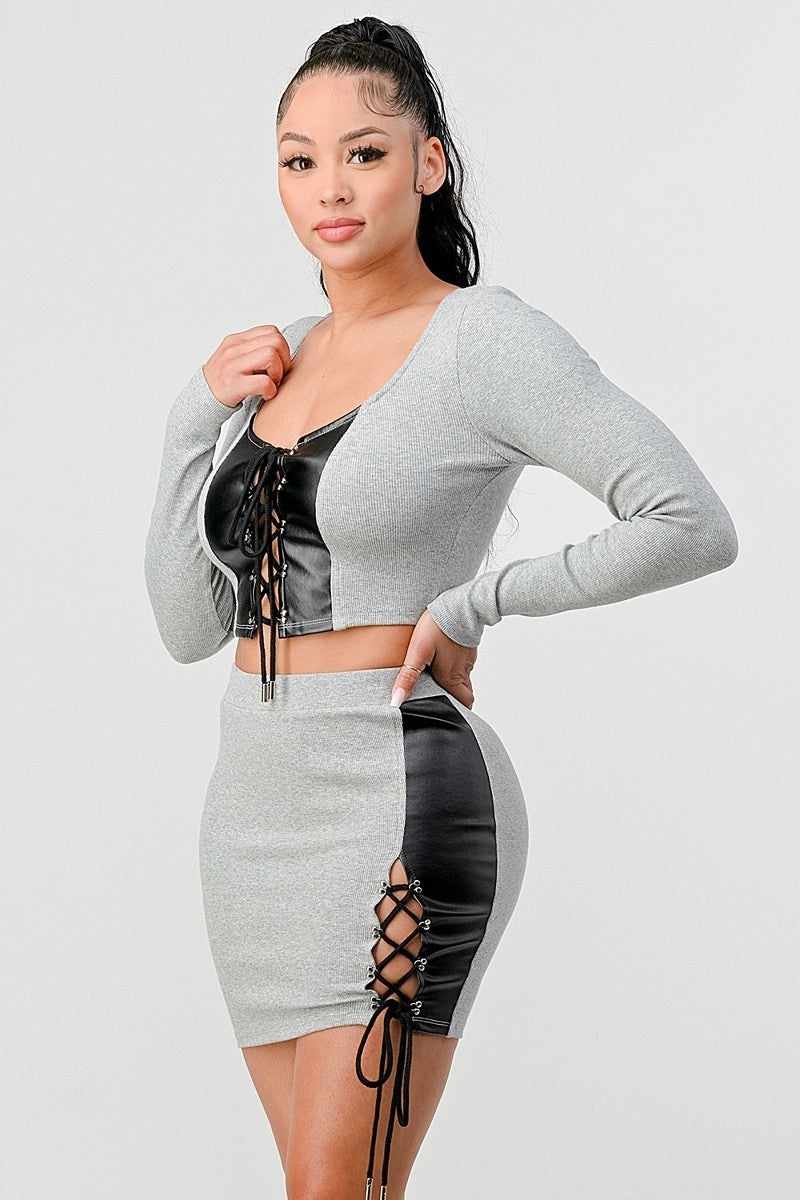 Woman wearing grey cropped long sleeve shirt and faux leather mini skirt set with crisscross lacing details.